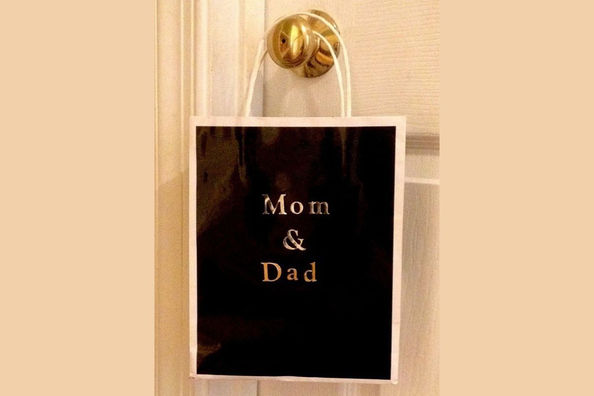A black gift bag with "Mom & Dad" written on it hangs from a white door knob, resembling the look of family mailboxes for special deliveries.