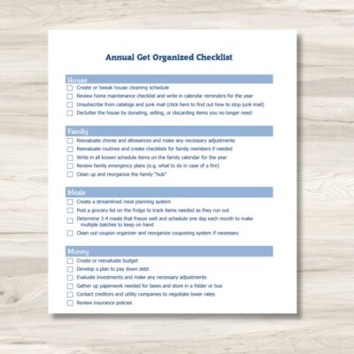A printed get organized checklist titled "Annual Get Organized Checklist" features sections for House, Family, Meals, and Money tasks, neatly placed on a light wooden surface.