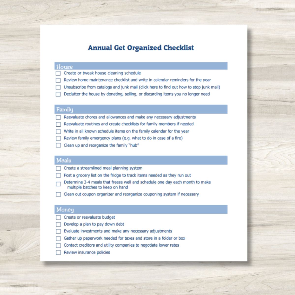 A printed get organized checklist titled "Annual Get Organized Checklist" features sections for House, Family, Meals, and Money tasks, neatly placed on a light wooden surface.