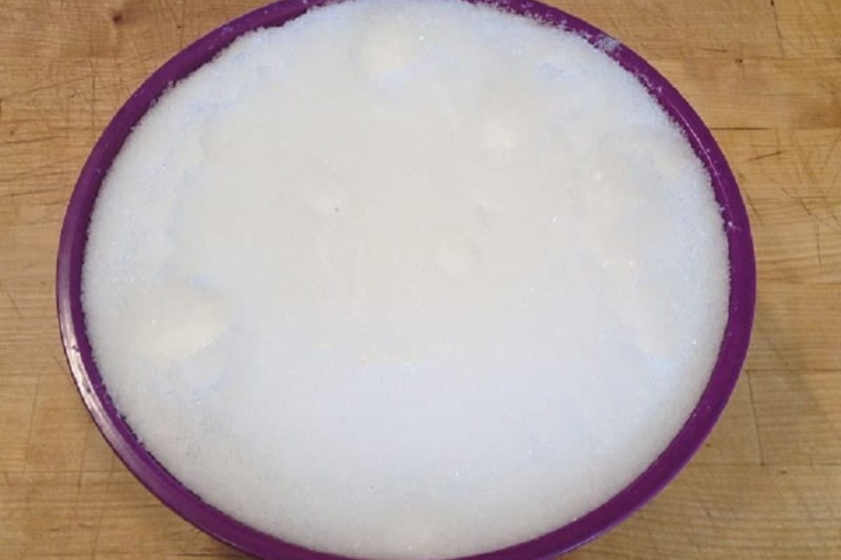 A purple bowl filled with white, snow ice cream-like soapy foam sits on a wooden surface.