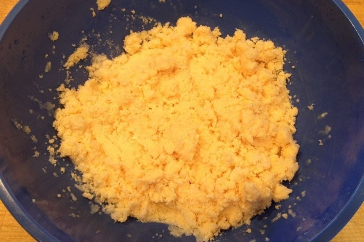 A blue mixing bowl filled with pale yellow, crumbly dough or pastry mixture, perfect for crafting homemade treats like snow ice cream.