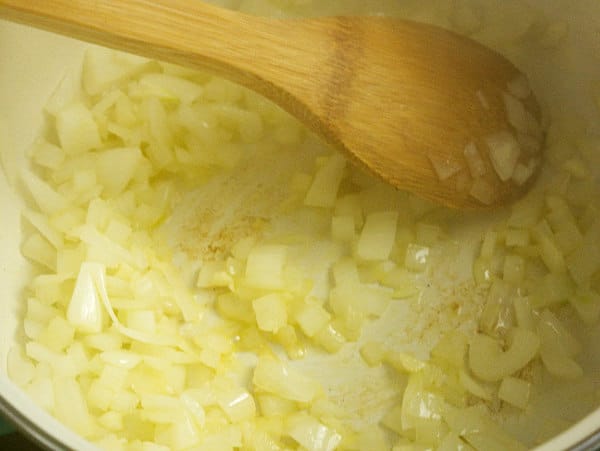 onions being sauteed using a wooden spoon in a pan