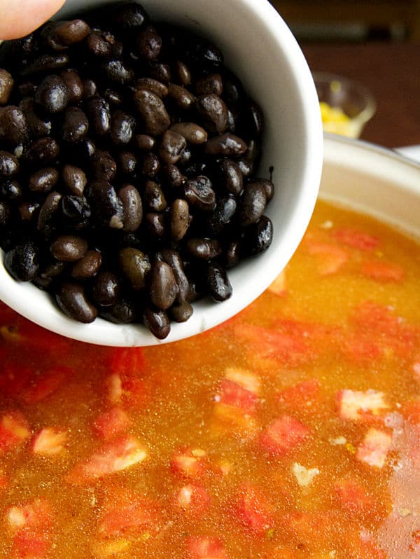 rinsed black beans being added to the tex mex chicken soup in a pot