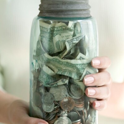 Woman holding glass jar pull of dollar bills and change