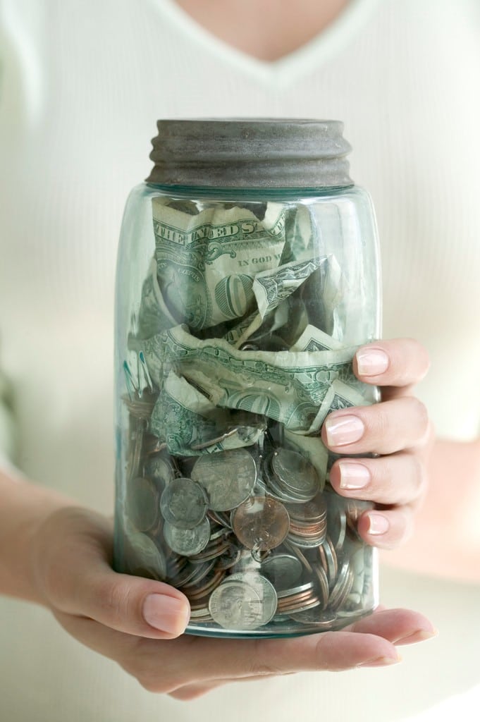 a person holding a jar full of dollar bills and coins using money saving tips