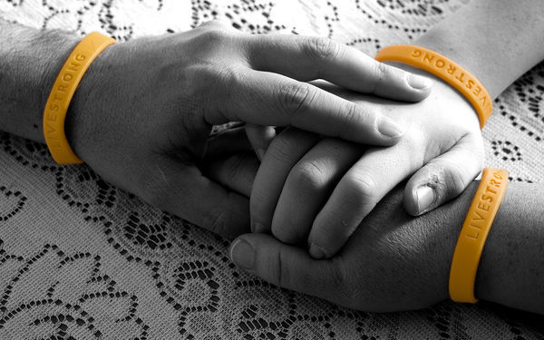 3 hands wearing orange live strong bracelets holding onto each other on a lace cloth
