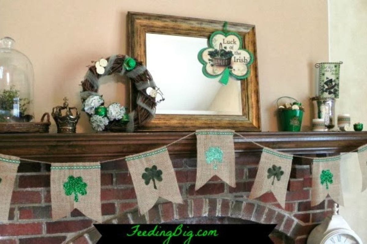 A brick fireplace mantel decorated with a shamrock banner, a clover wreath, St. Patrick's Day themed ornaments, and a plate of creme de menthe brownies, with a framed mirror above.