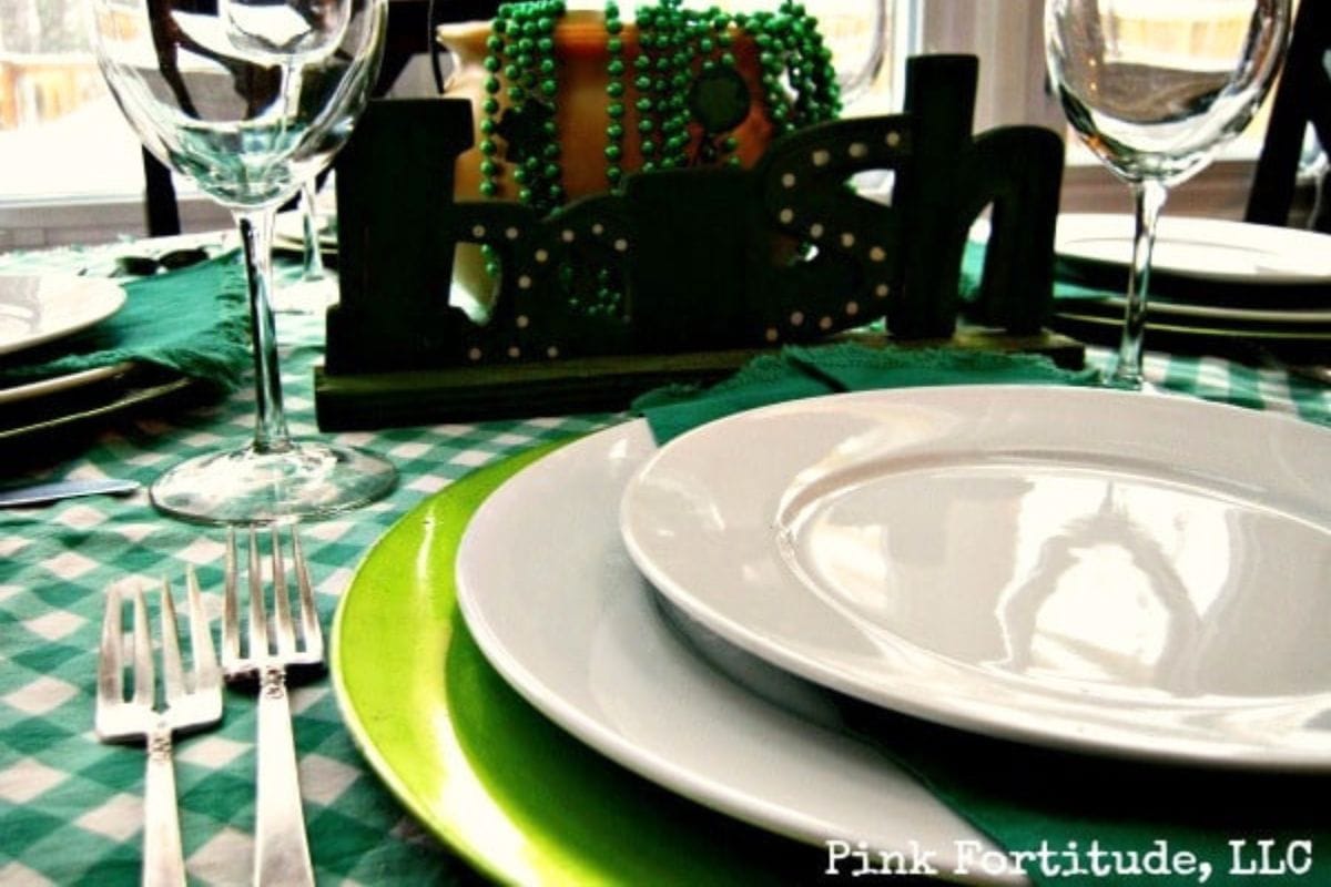 A table is set with white plates, green accents, wine glasses, and a centerpiece with "Irish," green beads, and creme de menthe brownies, suggesting a festive St. Patrick's Day theme.