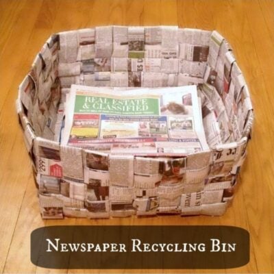 A rectangular newspaper basket, made from woven newspaper, sits on a wooden floor containing folded newspapers. Text overlay reads "Newspaper Recycling Bin.