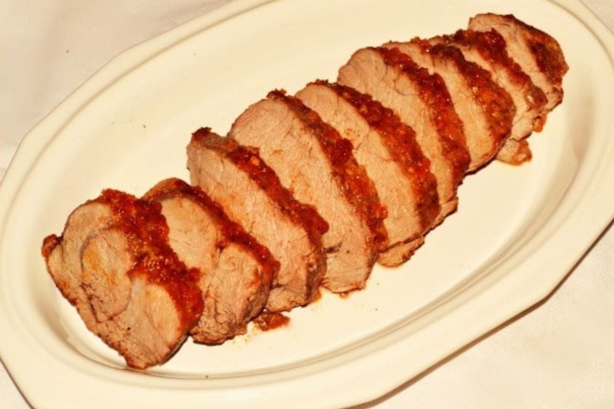 Sliced island pork tenderloin arranged on a white oval plate, topped with a rich reddish-brown sauce.