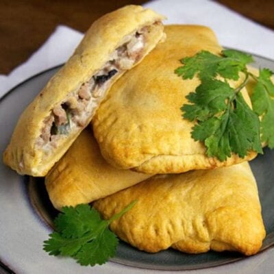 Three golden-brown ground turkey turnovers with savory filling sit on a plate, garnished with fresh cilantro. One turnover is cut open to reveal the flavorful filling inside.