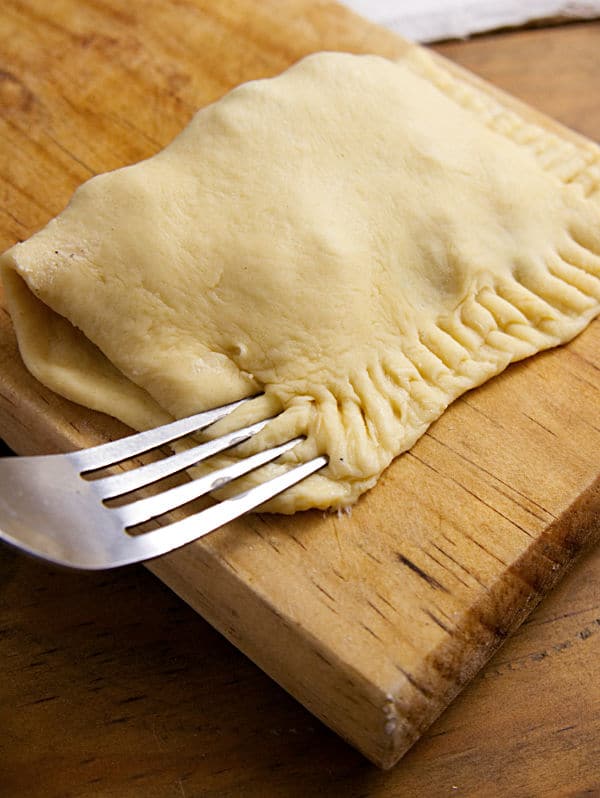a fork pressing down the edges of the dough of the turkey turnover on a wooden cutting board