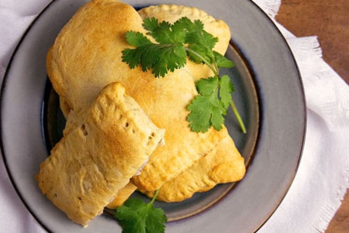 A plate with three golden-brown ground turkey turnovers topped with fresh cilantro, placed on a gray dish.