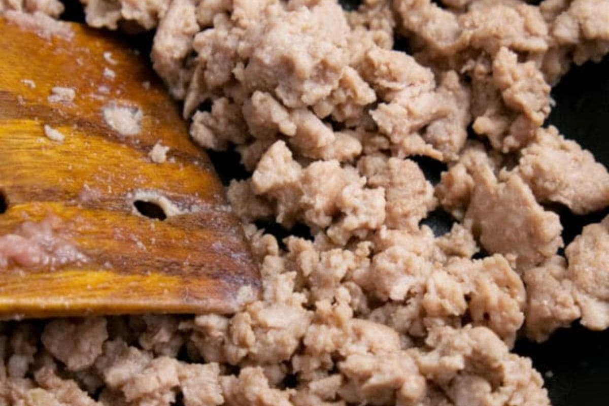 A wooden spatula stirring ground turkey cooking in a skillet.