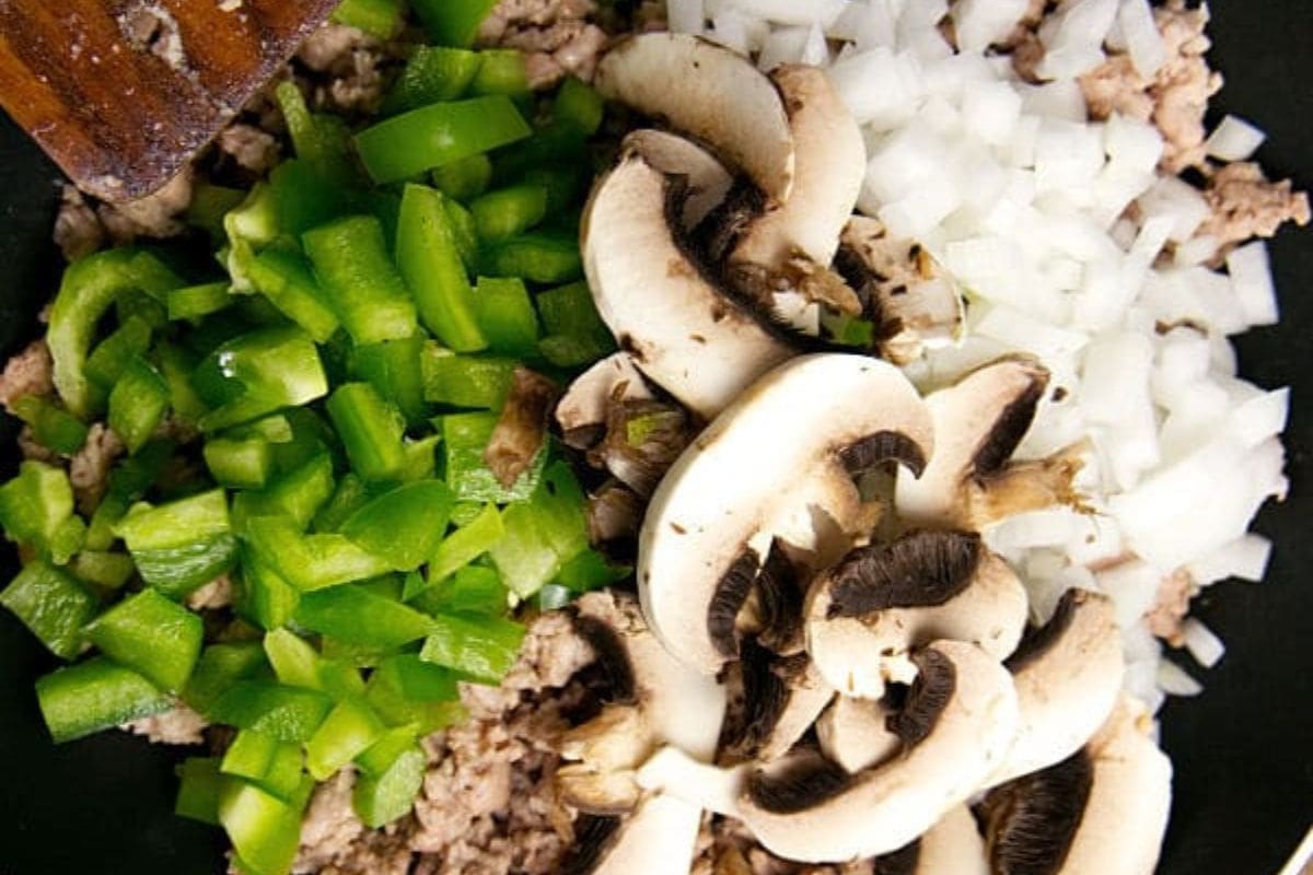 Diced bell pepper, mushrooms, onions, and ground turkey cooking in a skillet