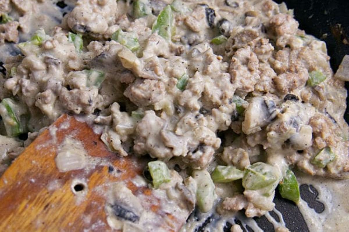 A wooden spatula stirring turkey mixture in a skillet.