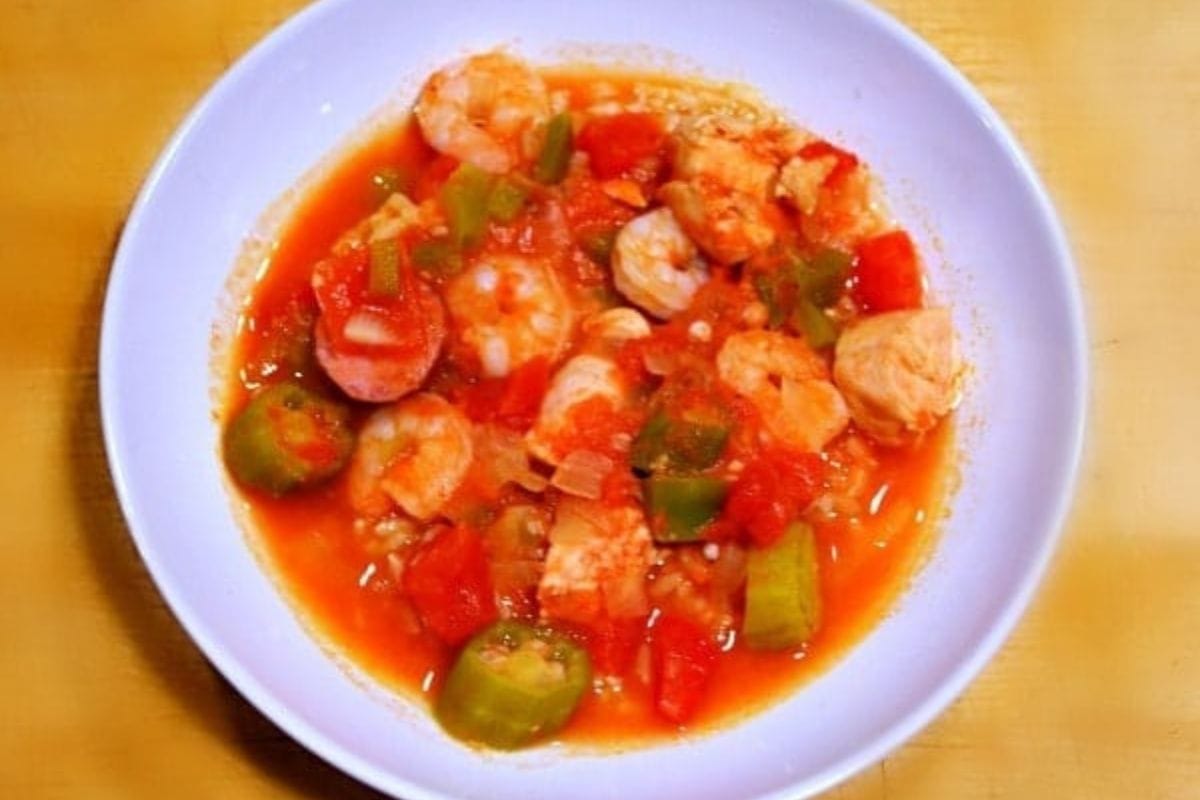 A bowl of jambalaya with shrimp, sausage, chicken, tomatoes, okra, and bell peppers in a red sauce on a white plate-perfect for those craving the hearty flavors of healthy gumbo.