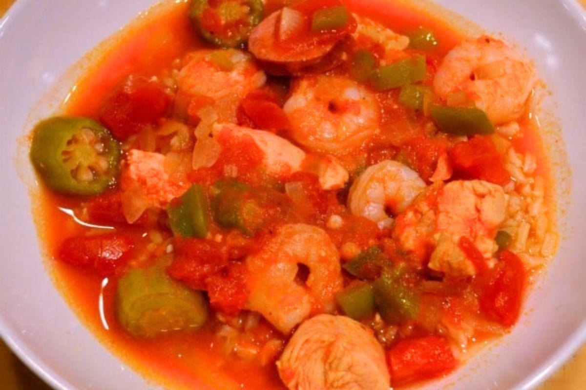 A bowl of jambalaya with shrimp, chicken, okra, green bell peppers, tomatoes, and rice in a red broth-perfect for fans of healthy gumbo flavors.