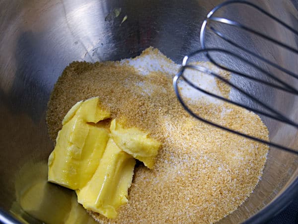 butter and sugars in a metal mixing bowl with whisks above it