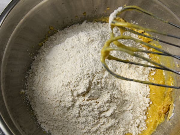 flour added to the cookie batter in a metal mixing bowl with whisks above it