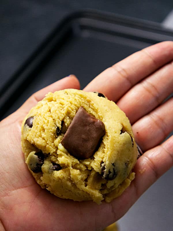 a hand holding cookie dough with a snickers bar in it