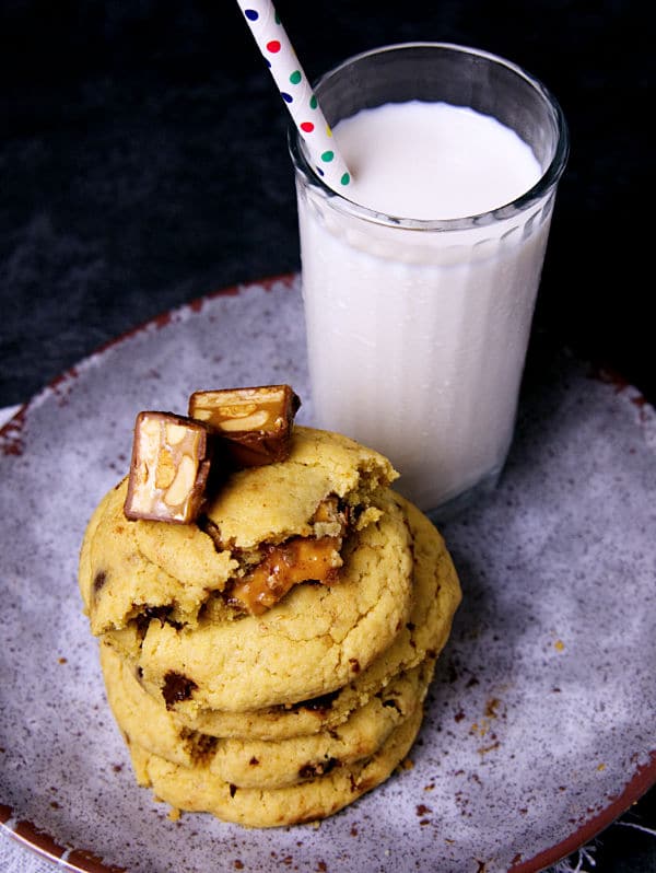 a stack of Snickers Cookies on a plate next to a glass of milk