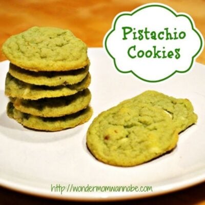 A plate with a stack of green pistachio cookies and two beside it. The text "Pistachio Cookies" highlights these delicious pistachio cookies, with the website URL featured at the bottom.