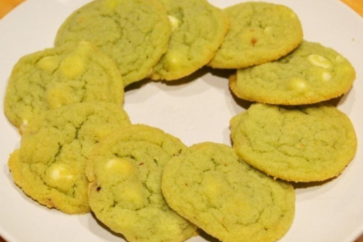 A plate with nine pistachio cookies containing white chocolate chips arranged in a circular pattern.