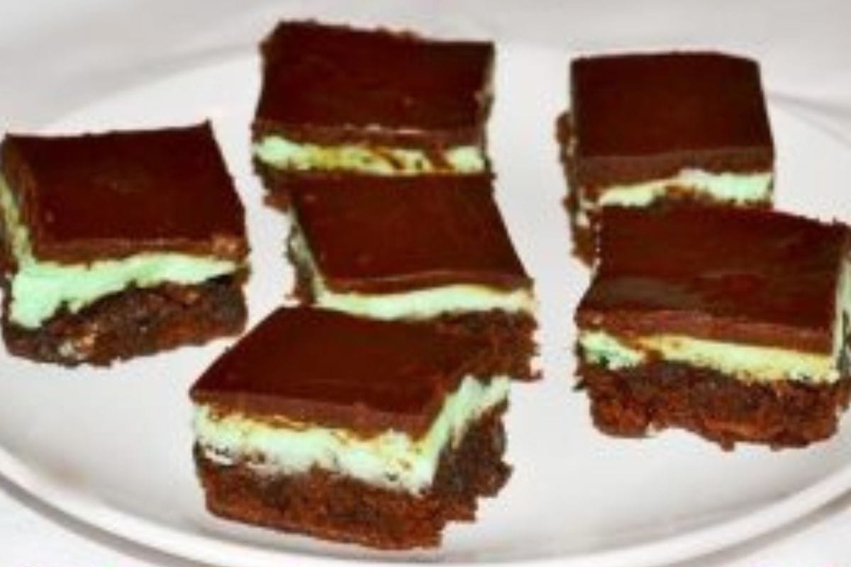 Six chocolate mint layered brownies are arranged on a white plate. The brownies have a green mint filling and a chocolate topping, making them the perfect treat alongside your favorite pistachio cookies.
