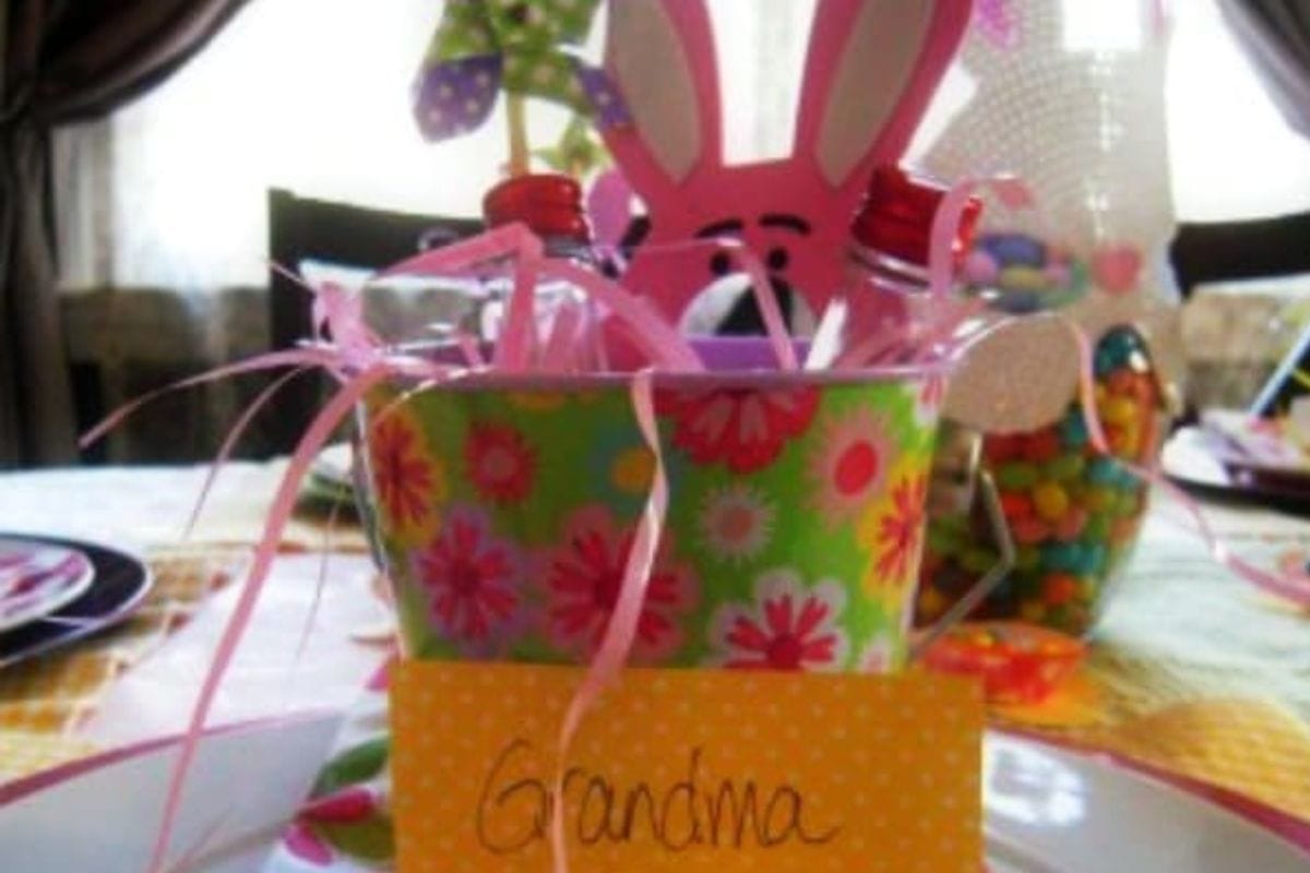 A floral Easter-themed gift basket with pink bunny ears, ribbons, and a "you've been egged" tag sits on a plate.