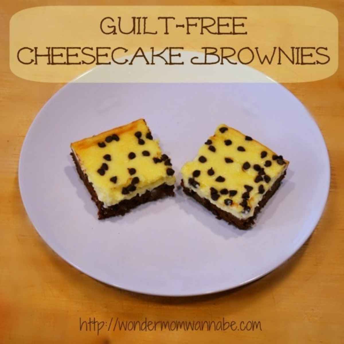 A white plate holds two guilt-free cheesecake brownies with chocolate chips, placed on a wooden surface. Text above reads "Guilt-Free Cheesecake Brownies.