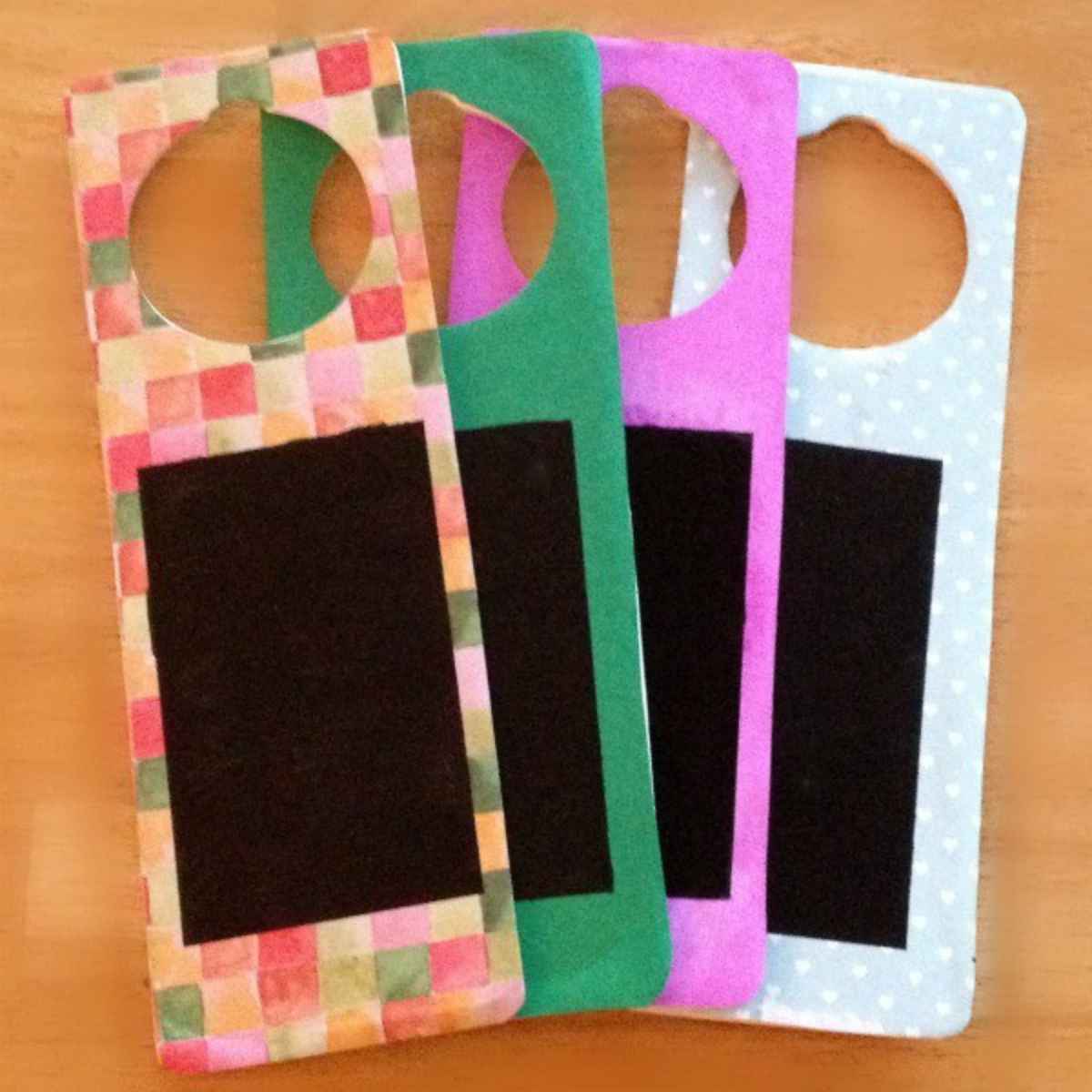 Four colorful DIY door hangers with black rectangular chalkboard sections, each featuring a circular cut-out at the top for easy hanging.