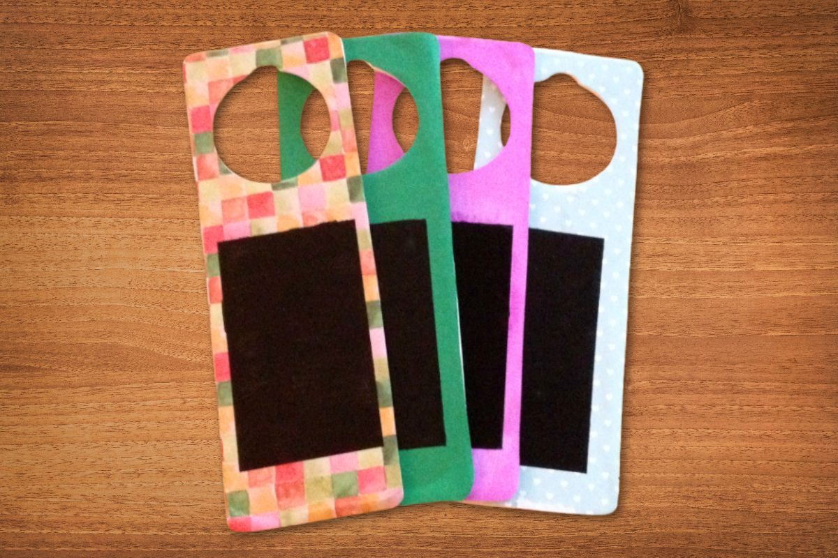 Four colorful DIY door hangers with black rectangular sections are arranged on a wooden surface.