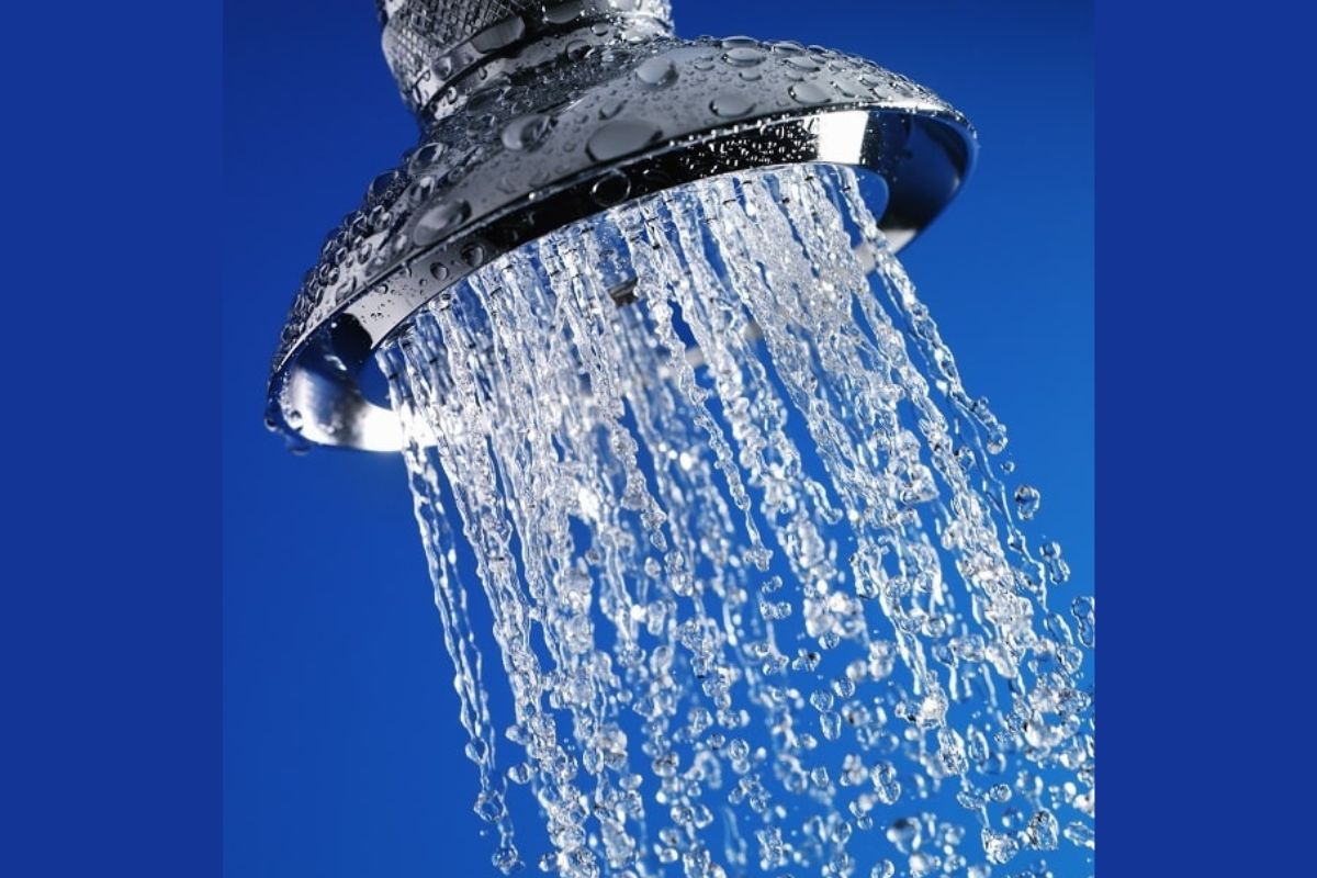 Close-up of a metal showerhead with water spraying out against a blue background.