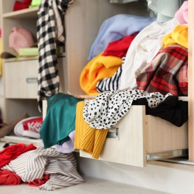 An open closet and drawer overflow with colorful clothes, garments spilling onto the floor in a lively jumble.