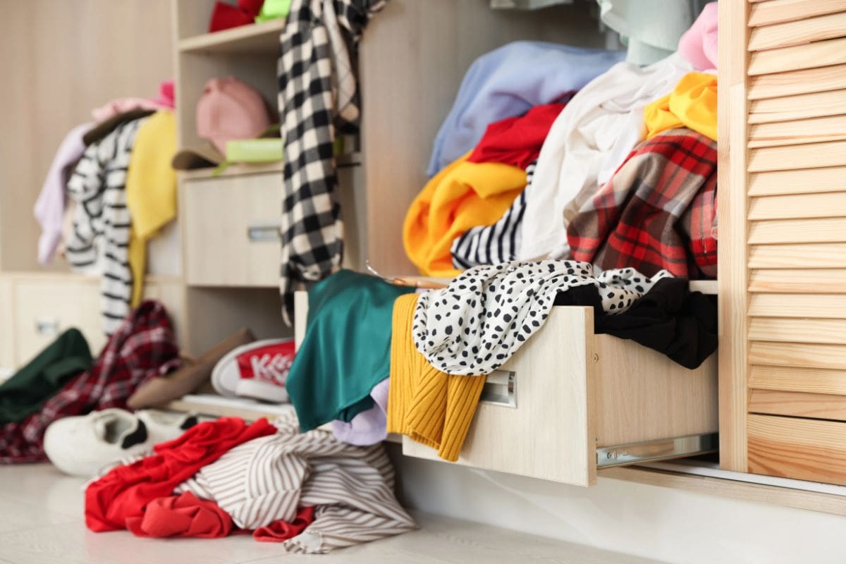 An open wardrobe drawer overflowing with various colorful clothes and fabrics.