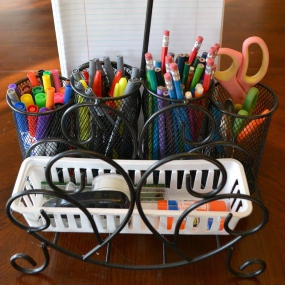 A desktop organizer enhances your study space, holding cups filled with pens, pencils, markers, scissors, and a white tray containing glue sticks, tape, and correction tape—all with a notepad in the background.