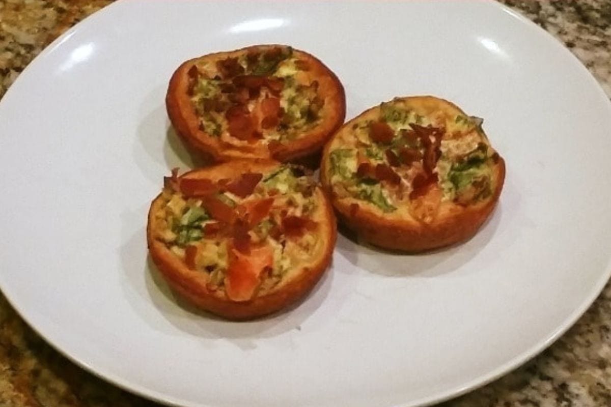 Three small, round BLT appetizer cups with visible bits of vegetables and bacon are arranged on a white plate.