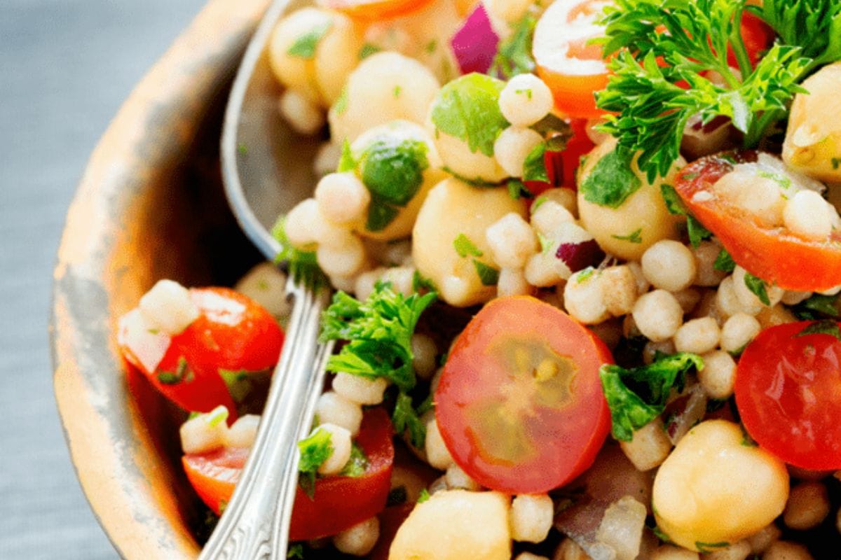 Close-up of a delicious carb cycling-friendly salad featuring pearl couscous, chickpeas, cherry tomatoes, parsley, red onion, and a spoon in a bowl.