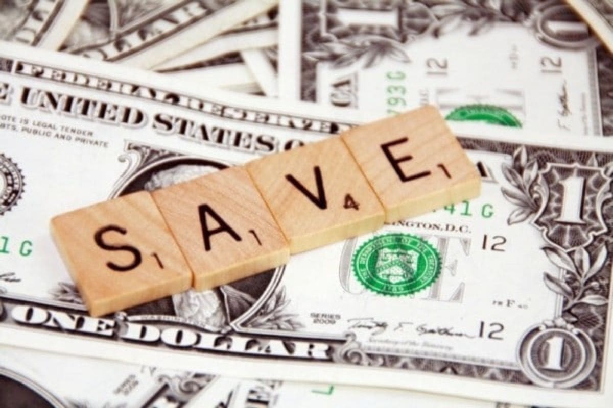Wooden Scrabble tiles spelling "SAVE" are placed on top of scattered U.S. one-dollar bills, symbolizing how you can save money on your utility bills.