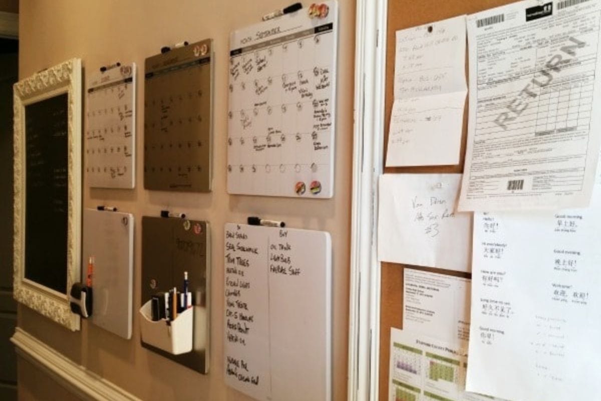 A wall in this organized home displays dry erase calendars, whiteboards with schedules, and a corkboard holding pinned papers, receipts, and charts along the hallway.