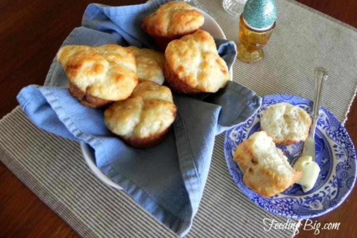 Rolls on a plate and in a dish with a cloth in it on a gray mat on a brown table.
