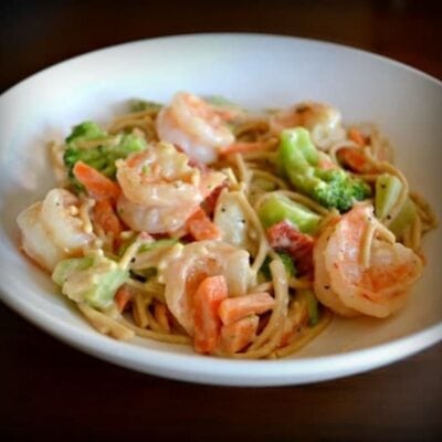 A white bowl filled with microwave shrimp primavera—spaghetti, shrimp, broccoli, and carrot slices in a creamy sauce.