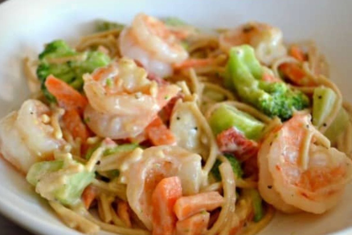 A bowl of microwave shrimp primavera pasta with broccoli, carrots, and a creamy sauce.