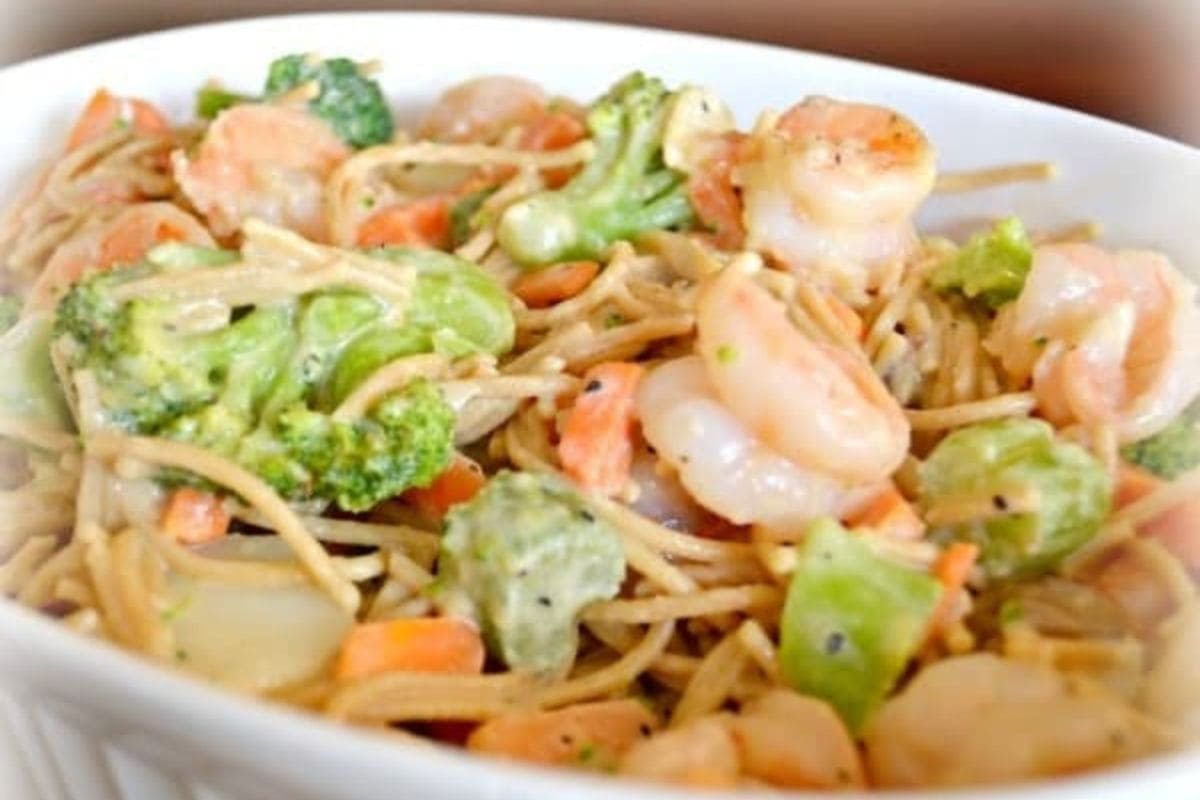 A bowl of microwave shrimp primavera pasta mixed with broccoli, carrots, and a creamy sauce.