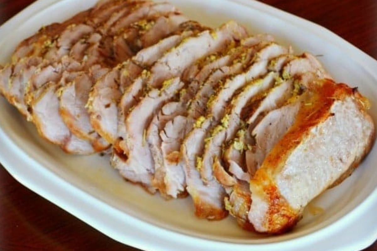 A white oval plate with several slices of herb roasted pork loin, arranged neatly in a row.