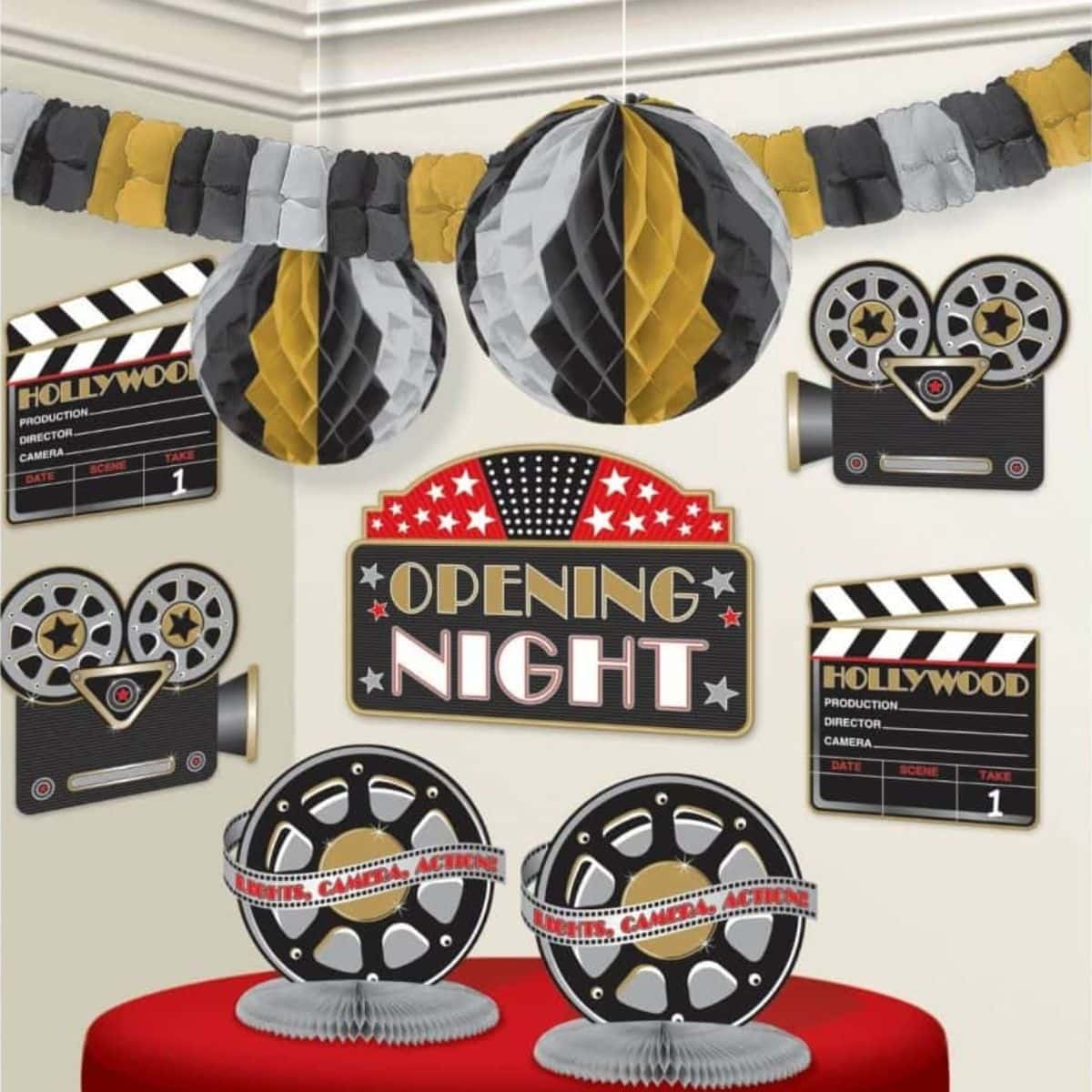 Movie party-themed decorations, including film reels, clapperboards, and an "Opening Night" sign, are arranged on a wall and table with black, gold, and silver paper garlands and hanging ornaments.