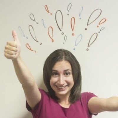 Woman smiling and giving a thumbs up, with colorful exclamation and question marks drawn on the wall behind her head—showcasing how positive gestures can improve your mood.
