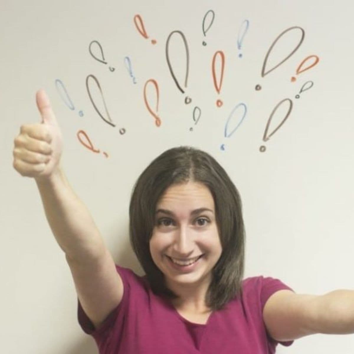 Woman smiling and giving a thumbs up, with colorful exclamation and question marks drawn on the wall behind her head—showcasing how positive gestures can improve your mood.