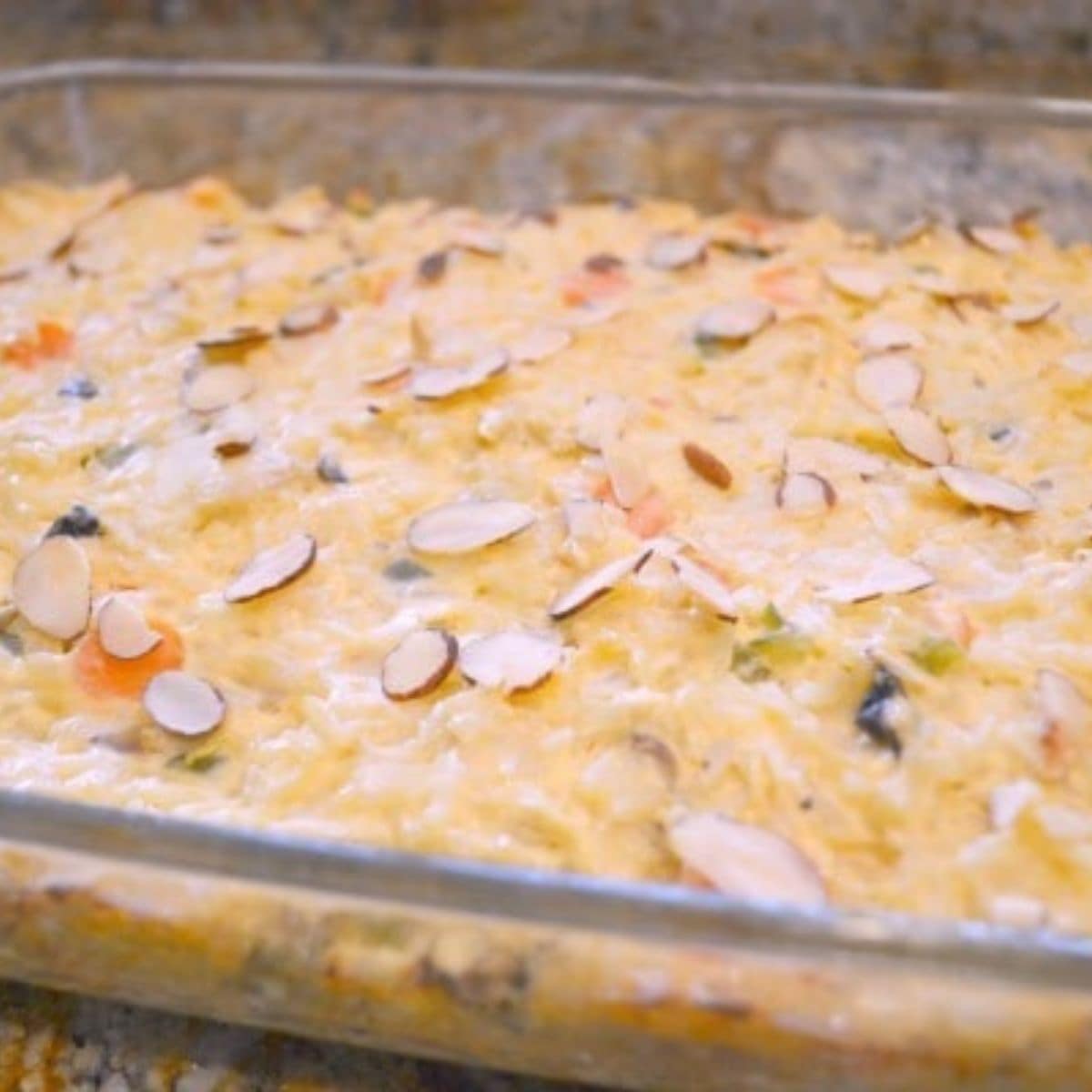 A glass baking dish filled with creamy garden chicken casserole, topped with sliced almonds.
